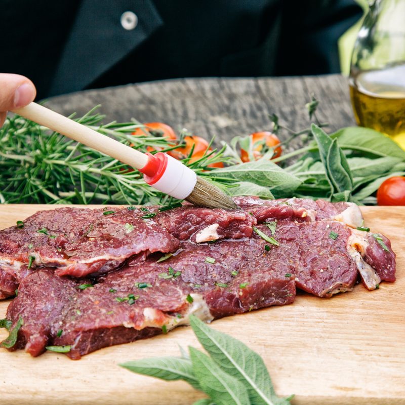 Cooking ingredients: marinated meat,oil,vinegar, herbs and vegetables. Chef is carving and marinating meat