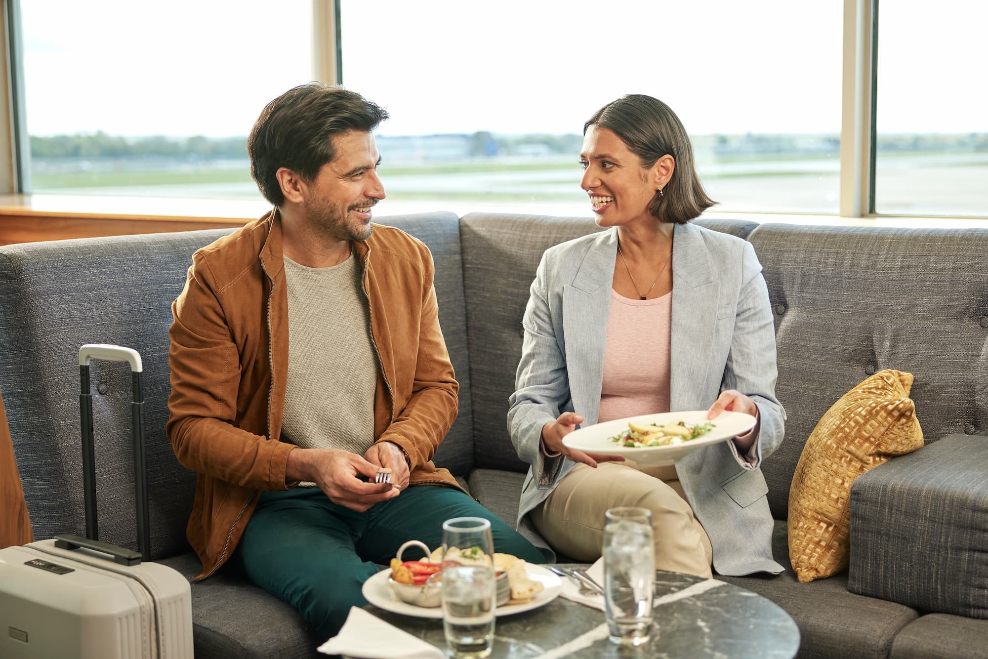 A man and a woman talking and eating in an airport lounge
