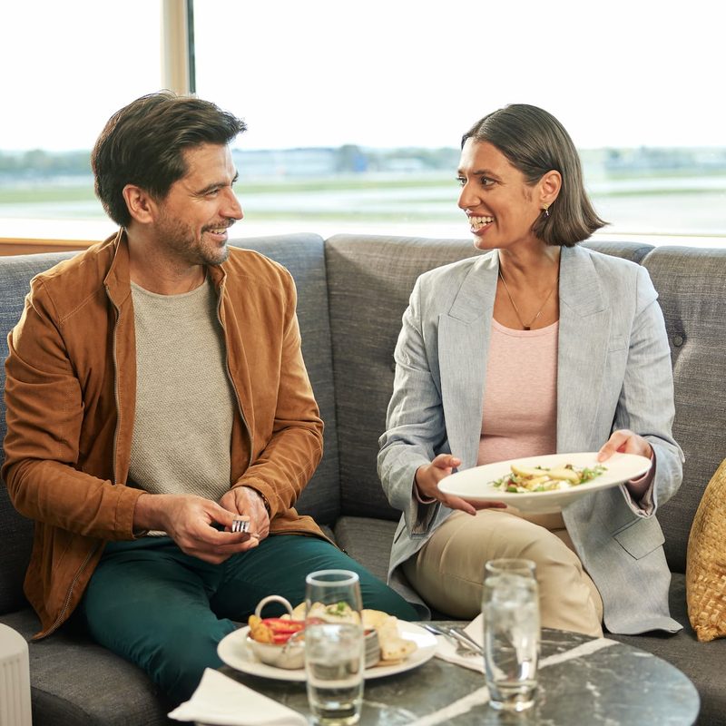 A man and a woman talking and eating in an airport lounge