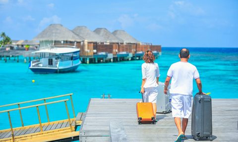 man and a woman walking on a dock by the ocean with rolling luggage