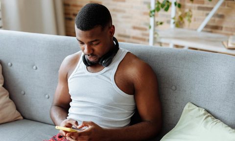 Man sitting on couch wearing headphones relaxing on phone