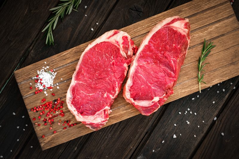 raw sirloin steak being prepared on wooden board