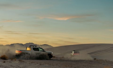 Two limited-edition Rivian California Dune trucks driving through the desert at dusk.