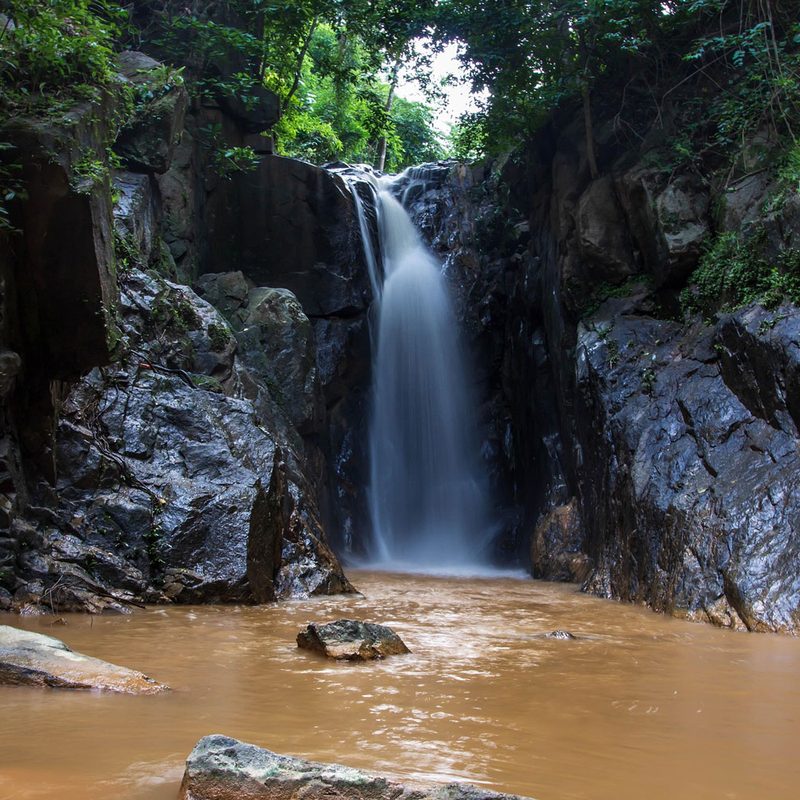 Small waterfall flowing into a dirty, brown river in the jungle