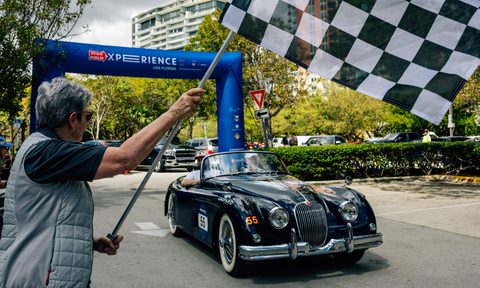 A Jaguar XK150 S crossing the finish line at the 1000 Miglia Experience Florida with a checkered flag waving