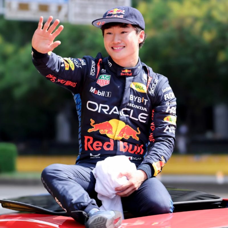 Yuki Tsunoda wearing a Red Bull shirt waving in 2024.