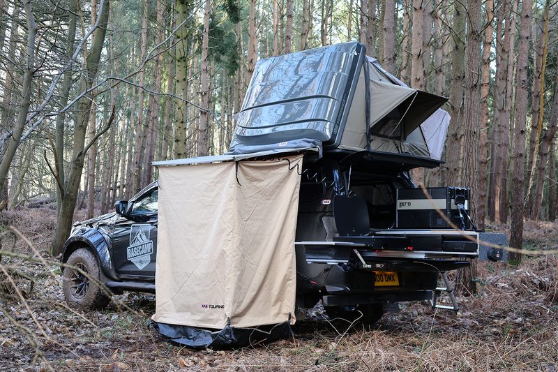 Rear view of an Isuzu Basecamp truck camper setup for camping in the woods.