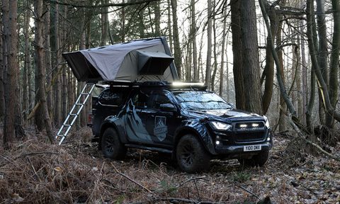 An Isuzu Arctic Trucks Basecamp truck camper parked in the woods with rooftop tent deployed.