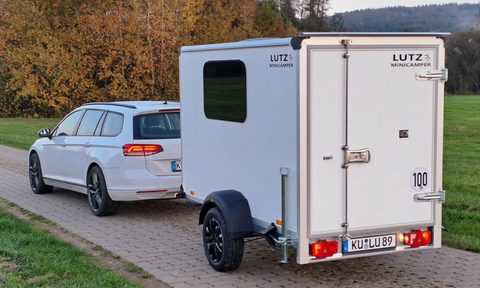 Lutz Minicamper travel trailer hitched up to a white Volkswagen.