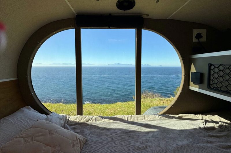 Panoramic window overlooking the ocean from inside a Naledi Campers teardrop travel trailer.
