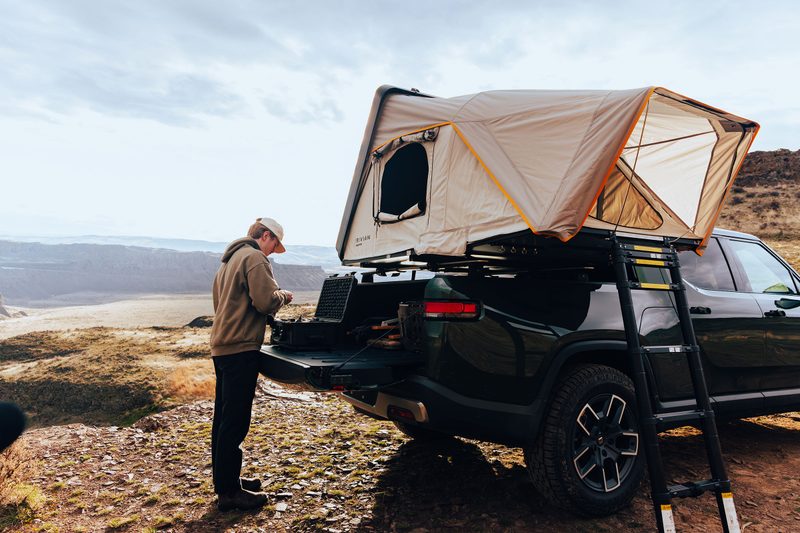 Man standing next to a Rivian x iKamper Skycamp Mini rooftop tent mounted to an R1T pickup truck.