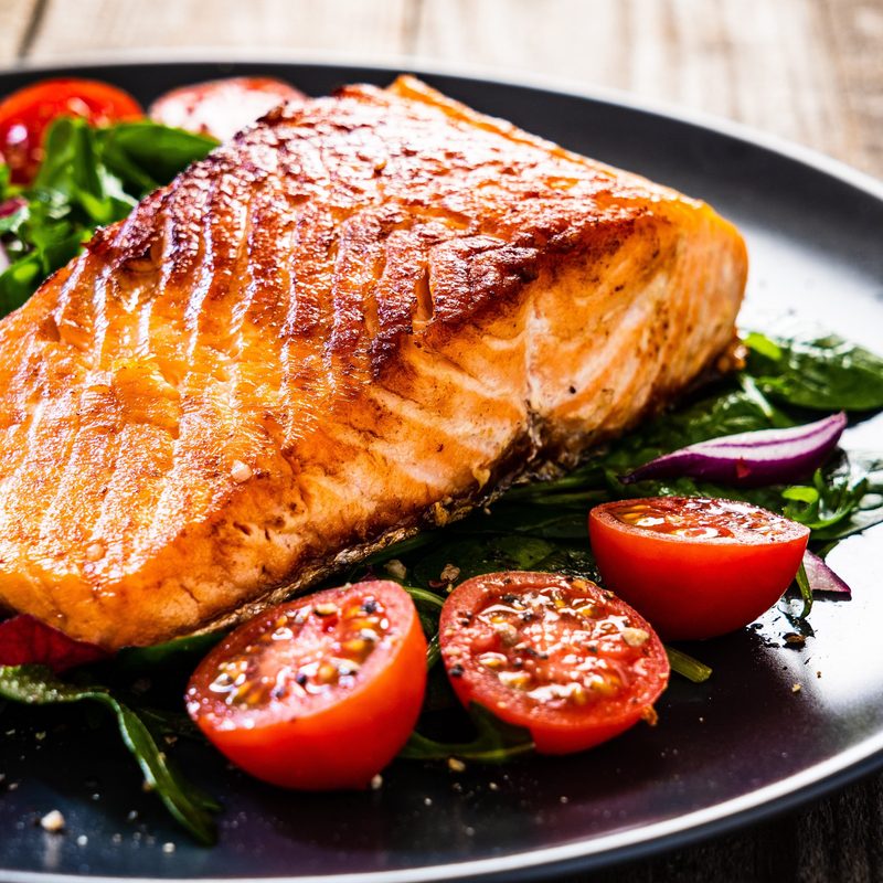 Fried salmon steak with vegetables on wooden table