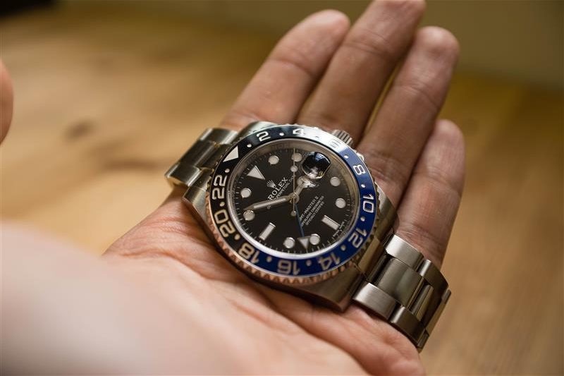 Rolex GMT Master II on a hand in front of a wood grain background.
