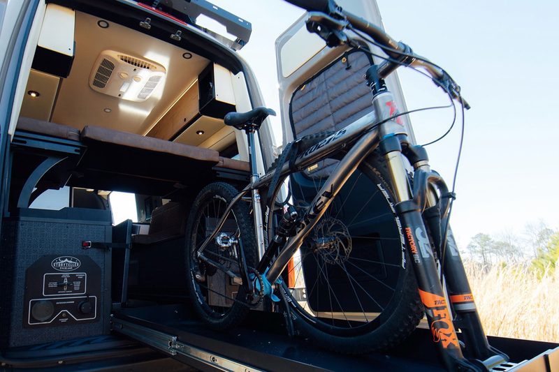 Mountain bike on the sliding gear tray of a Storyteller Overland Crew Mode adventure van.