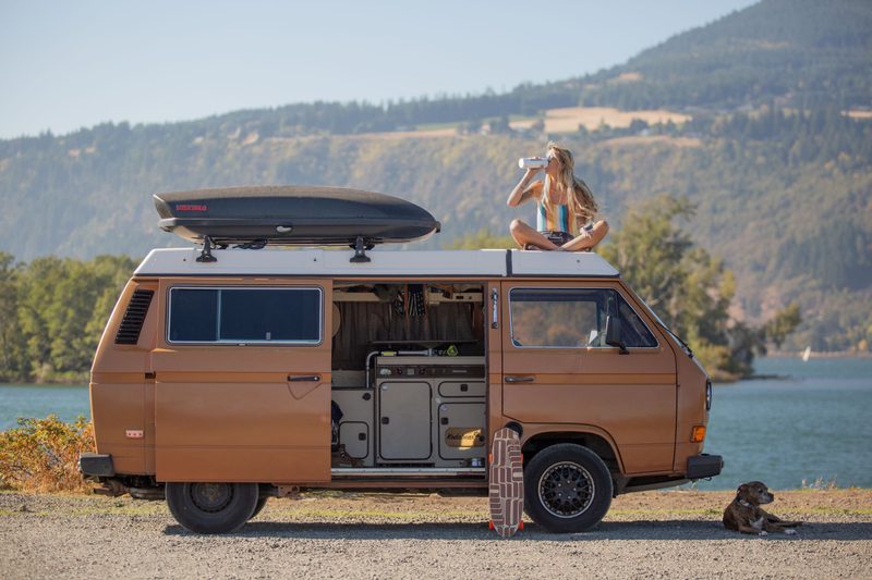 woman sitting on roof of van drinking a protein shake