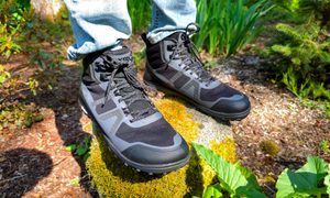 A man wearing Xero shoes while standing on a mossy rock