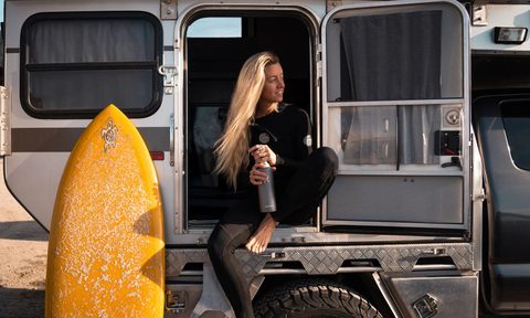 woman with surfboard drinking protein shake
