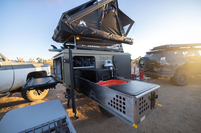 A Bean Pod adventure trailer with its rooftop tent and outdoor camp kitchen set up.
