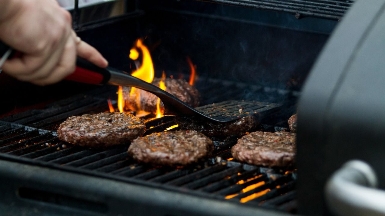 Someone using a spatula to smash burgers on a grill