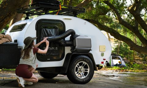 A camper setting up an EcoFlow Wave 3 portable air conditioner outside a small teardrop travel trailer.