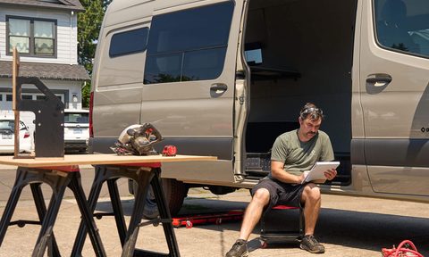 Man sitting inside an Outside Van Baseline campervan build in a driveway.