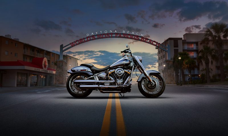 2025 Harley Davidson Fat Boy Gray Ghost right profile with Daytona Beach street scene background.