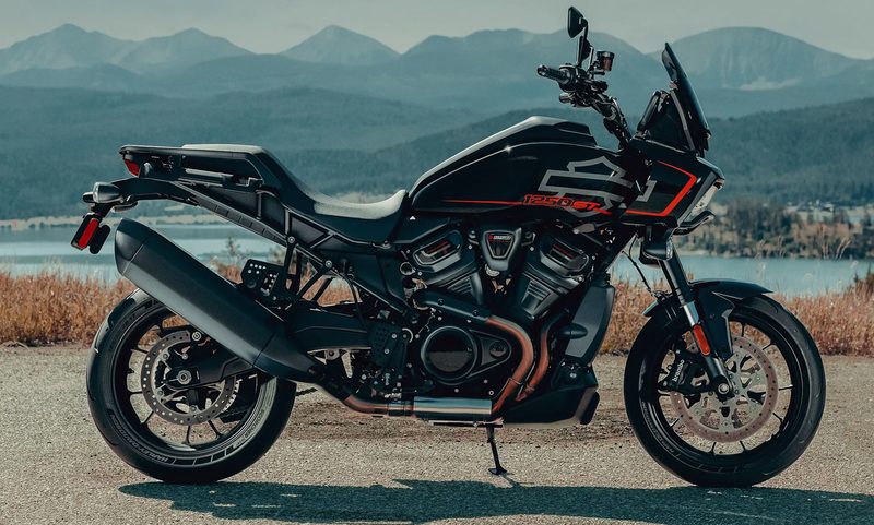 2025 Harley Davidson Pan America 1250 ST parked on pavement with a lake and mountains in the background.