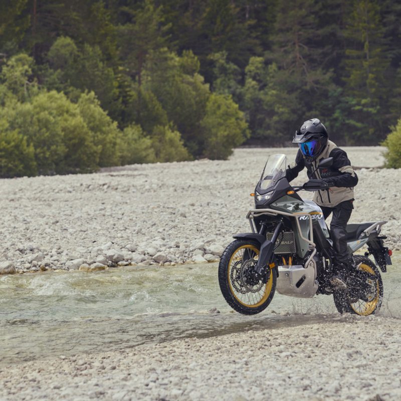 A single rider on a 2025 Honda XL750 Transalp driving adjacent to a stream between sandy ground.