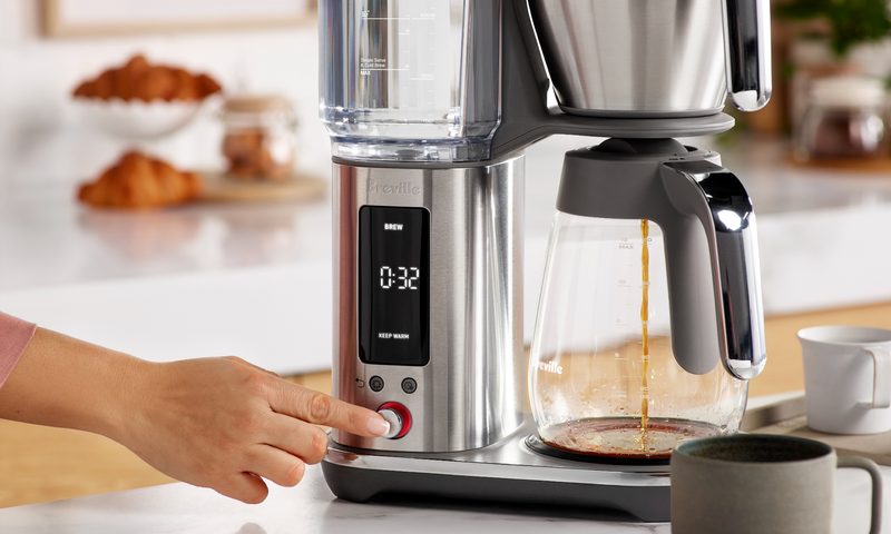 Pushing the brew button to start the coffee brewing with the Breville Luxe Brewer with glass carafe on a kitchen counter.