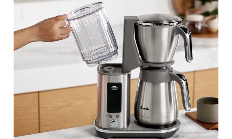 Removing the water reservoir from the Breville Luxe Brewer with thermal carafe on a kitchen counter.