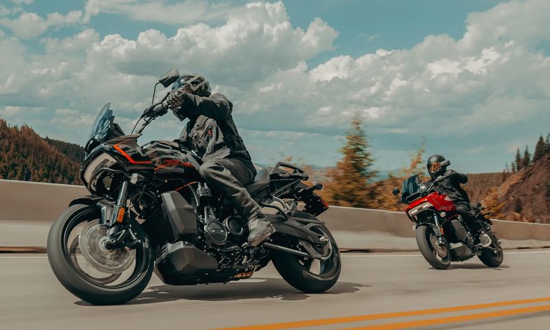 Two 2025 Harley Davidson Pan America 1250 STs on a curving road with mountains in the background.