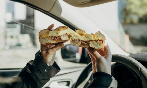 person holding a bagel sandwich in a car