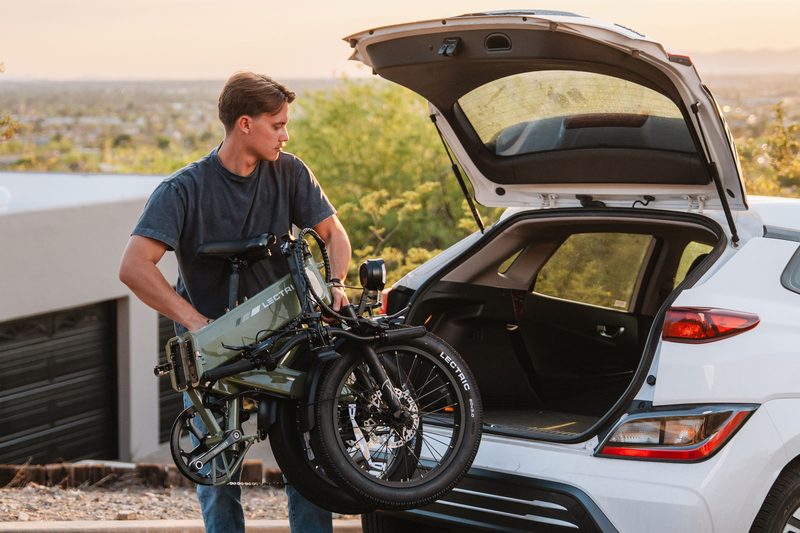 Man putting a folded-up Lectric XP4 electric bike into the back of a white vehicle.