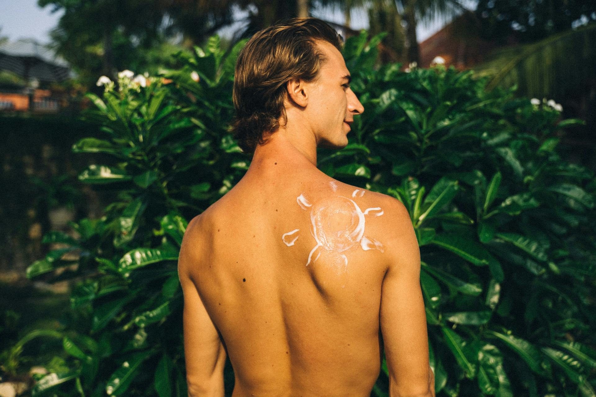 shirtless man with sunscreen on back in shape of sun