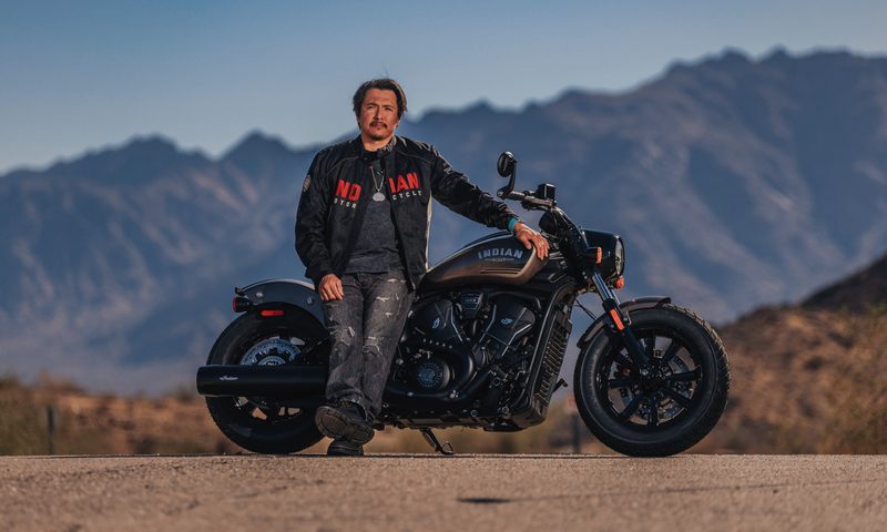 A rider wearing Arviso streetwear leaning on an Indian Motorcycle.