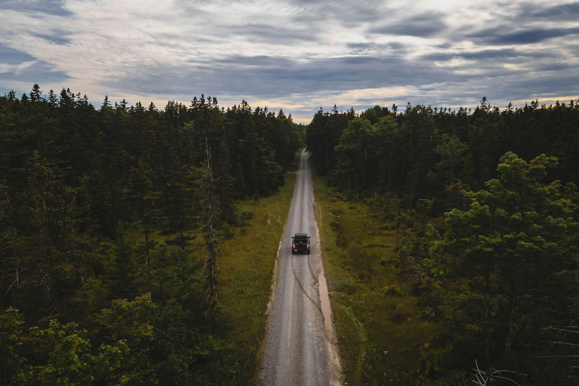 Aerial of an overlanding truck driving a long, straight dirt road.