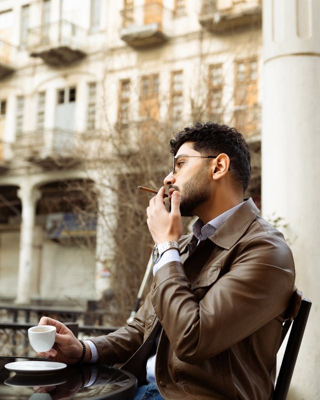 a bespectacled young man smoking a cigar at a cafe