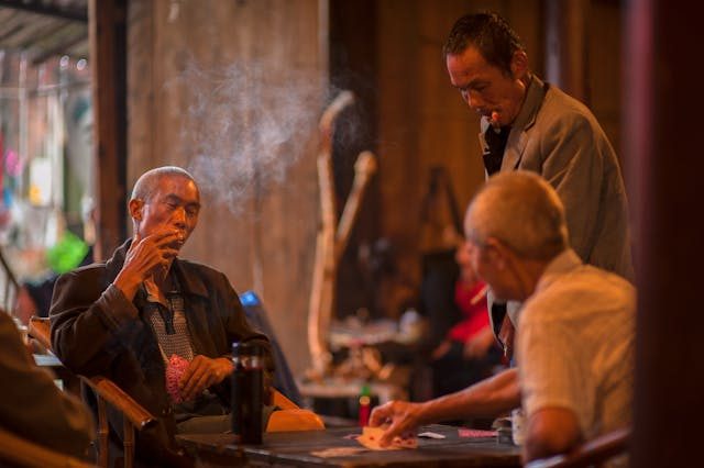 three elderly men smoking cigars while playing a card game