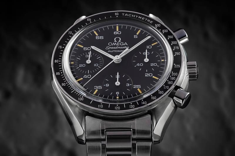 close up on a vintage Omega Speedmaster Automatic luxury wrist watch, background is a blurred rock texture.