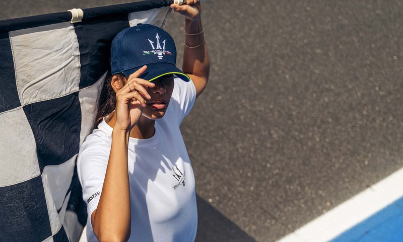 A model holding a race track checkered flag wearing a shirt and hat from the Sparco X Maserati fan collection.