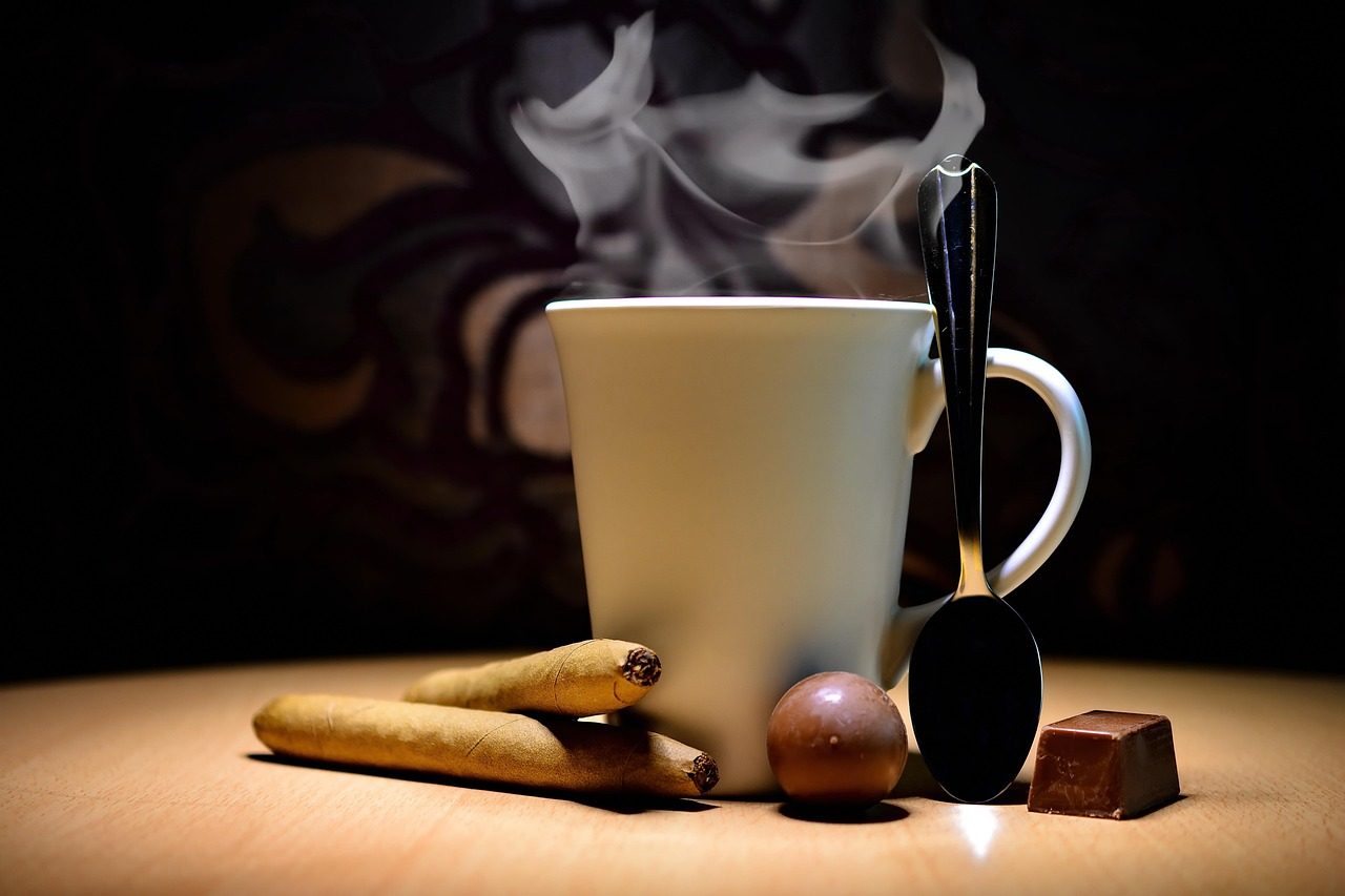 A cup of a hot drink next to chocolates and cigars