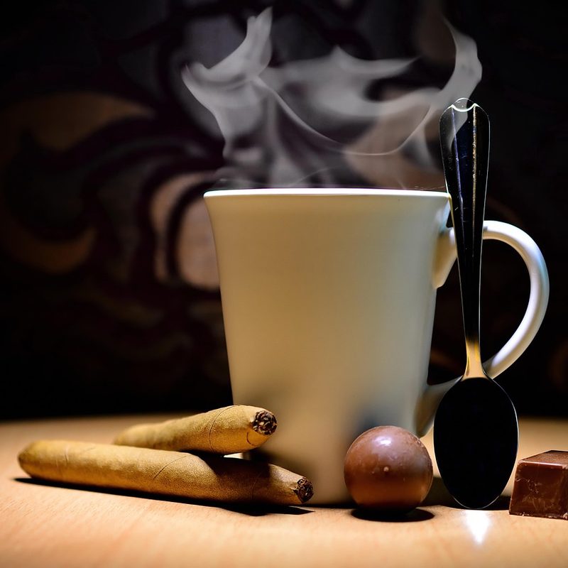 A cup of a hot drink next to chocolates and cigars