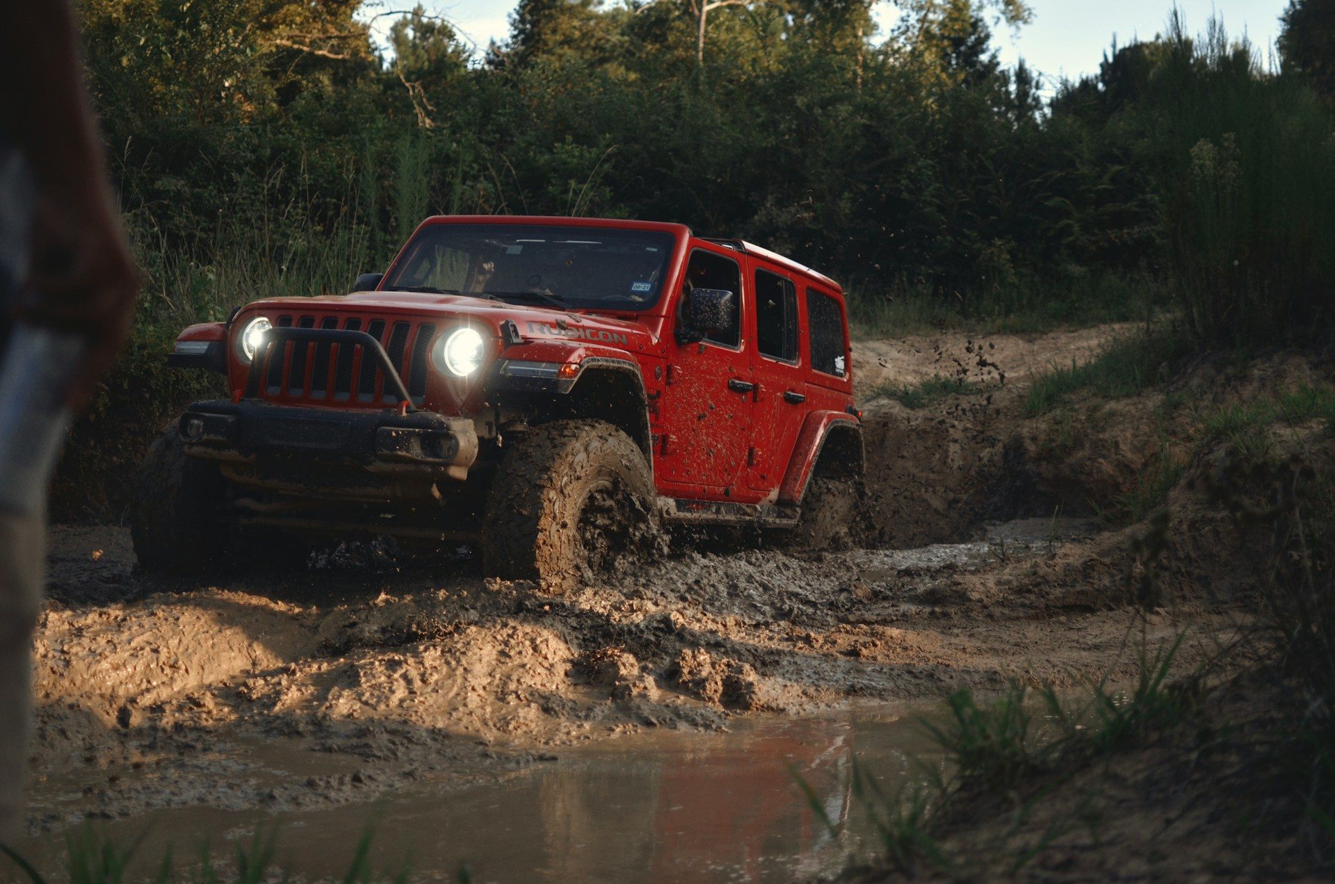 Red Jeep driving through deep mud on an off-road trail.