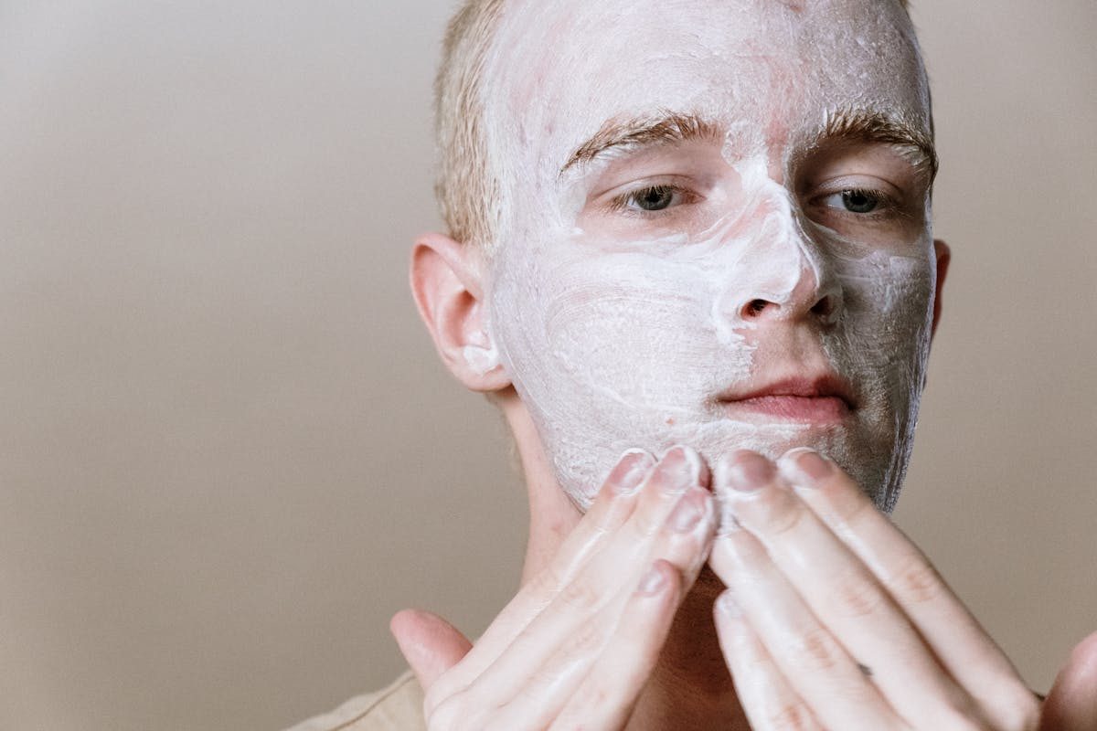 a man putting white cream all over his face with hands