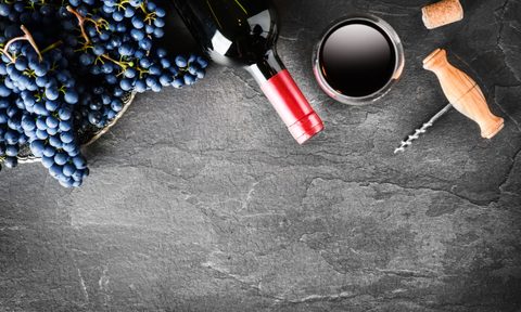 Red wine bottle and full glass, grapes on dark stone table top view. Vine concept on black background.