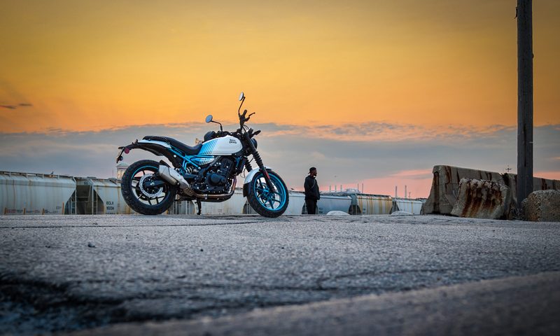 Royal Enfield Guerilla 450 right profile parked on asphalt with water and a dramatic sunset in the background.