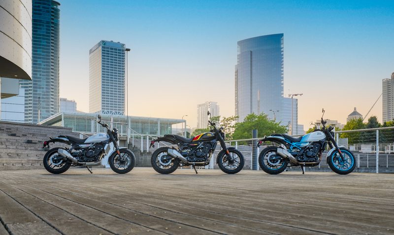 Three Royal Enfield Guerilla 450s right profile parked on a wooden walkway with city skyline in the background.