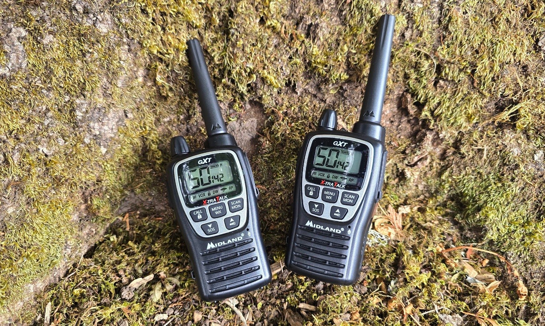 Two radios sitting on a mossy tree stump outside