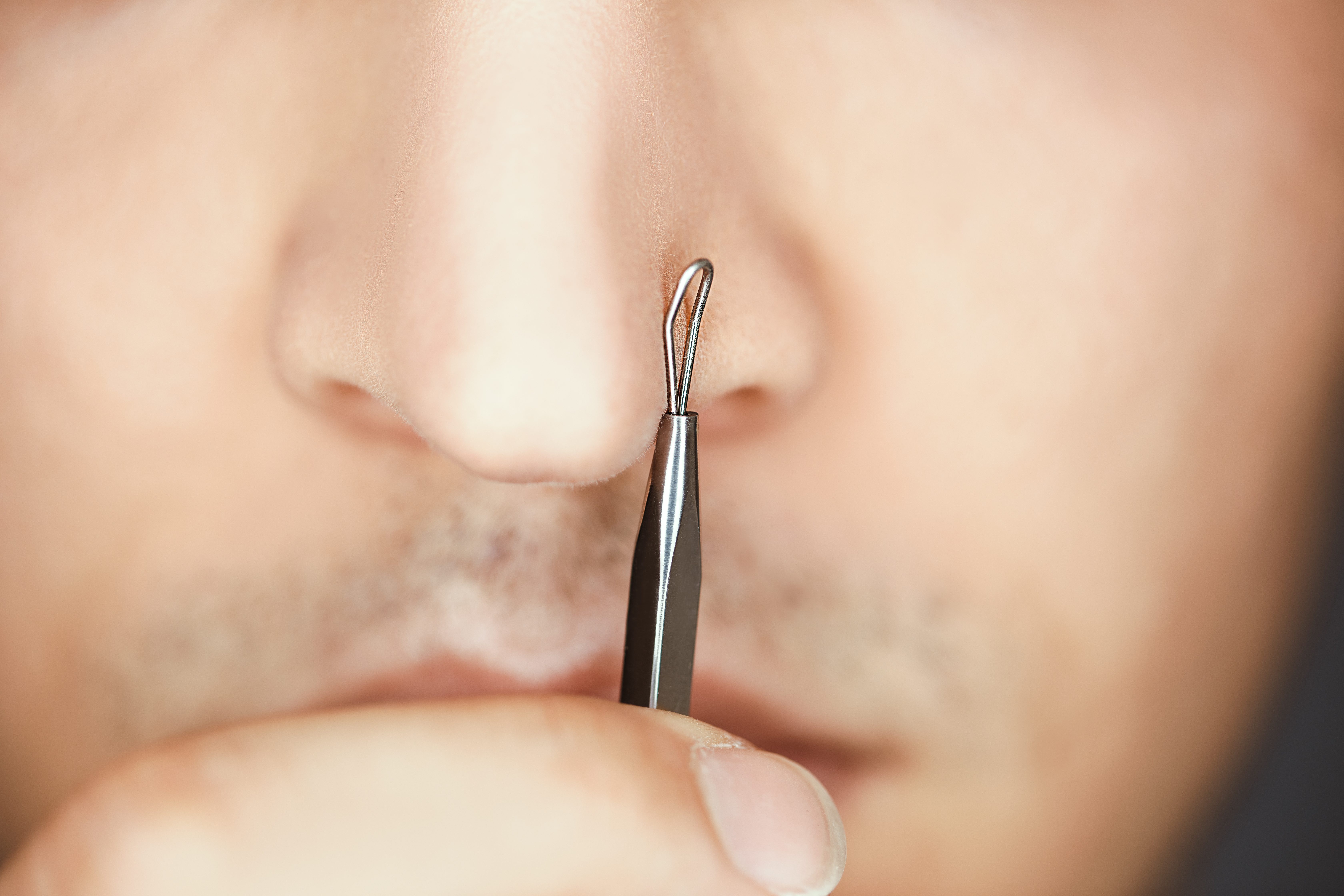 Man holding pimple popper tool to nose