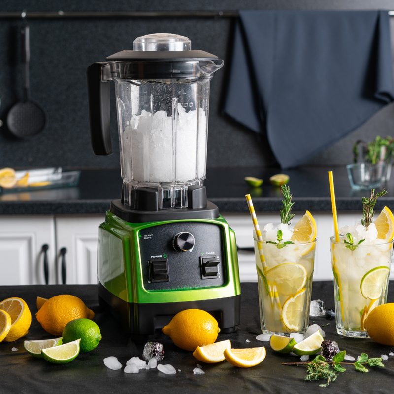 Wireless modern blender with blended ice inside the bowl. Making a healthy summer drink from citrus fruits. Lemon, lime, mint and ice.